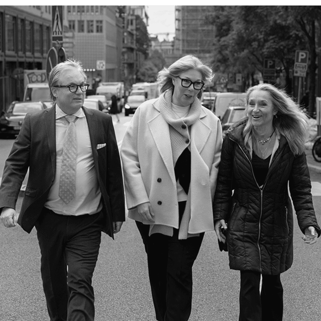 Tre personer går bredvid varandra på en fartfylld gata. De pratar och ser glada ut.