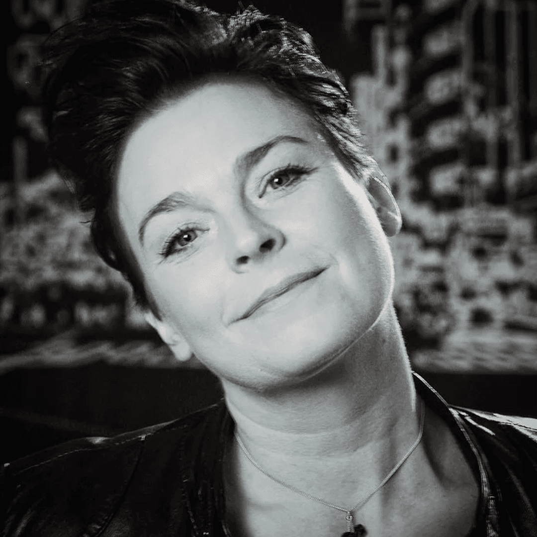 Kvinna med kortklippt hår, huvud på sne. Ler diskret och tittar in mot kameran.