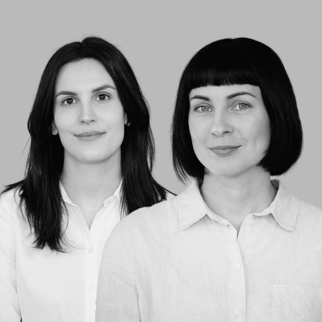 Bild på två kvinnor. En med axellångt hår och den andra med page. Båda bär vita skjortor.