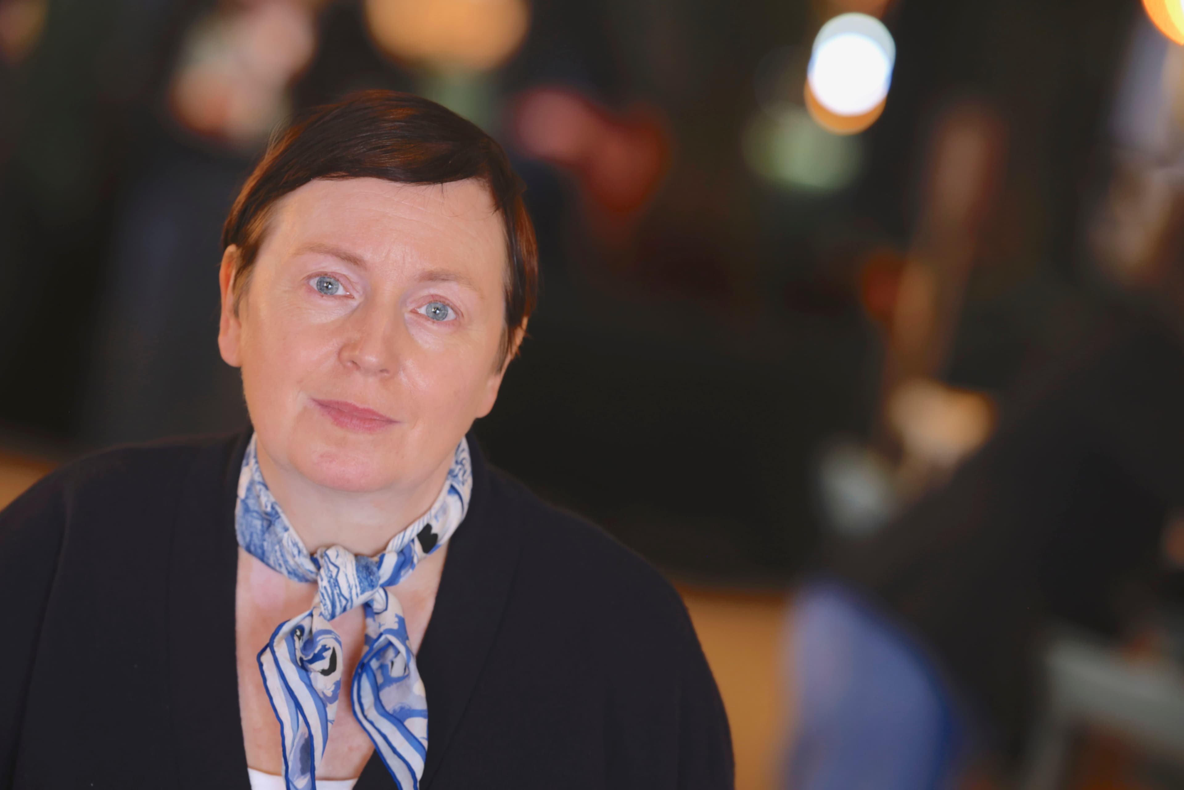 Kortklippt kvinna med mörkt hår, svart kavaj och scarf.