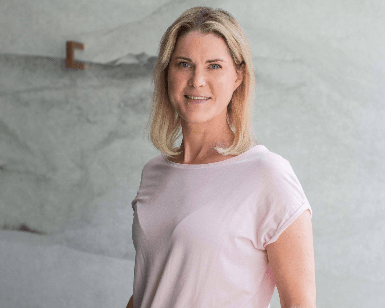 Blond kvinna tittar in i kameran. Ljus bakgrund.