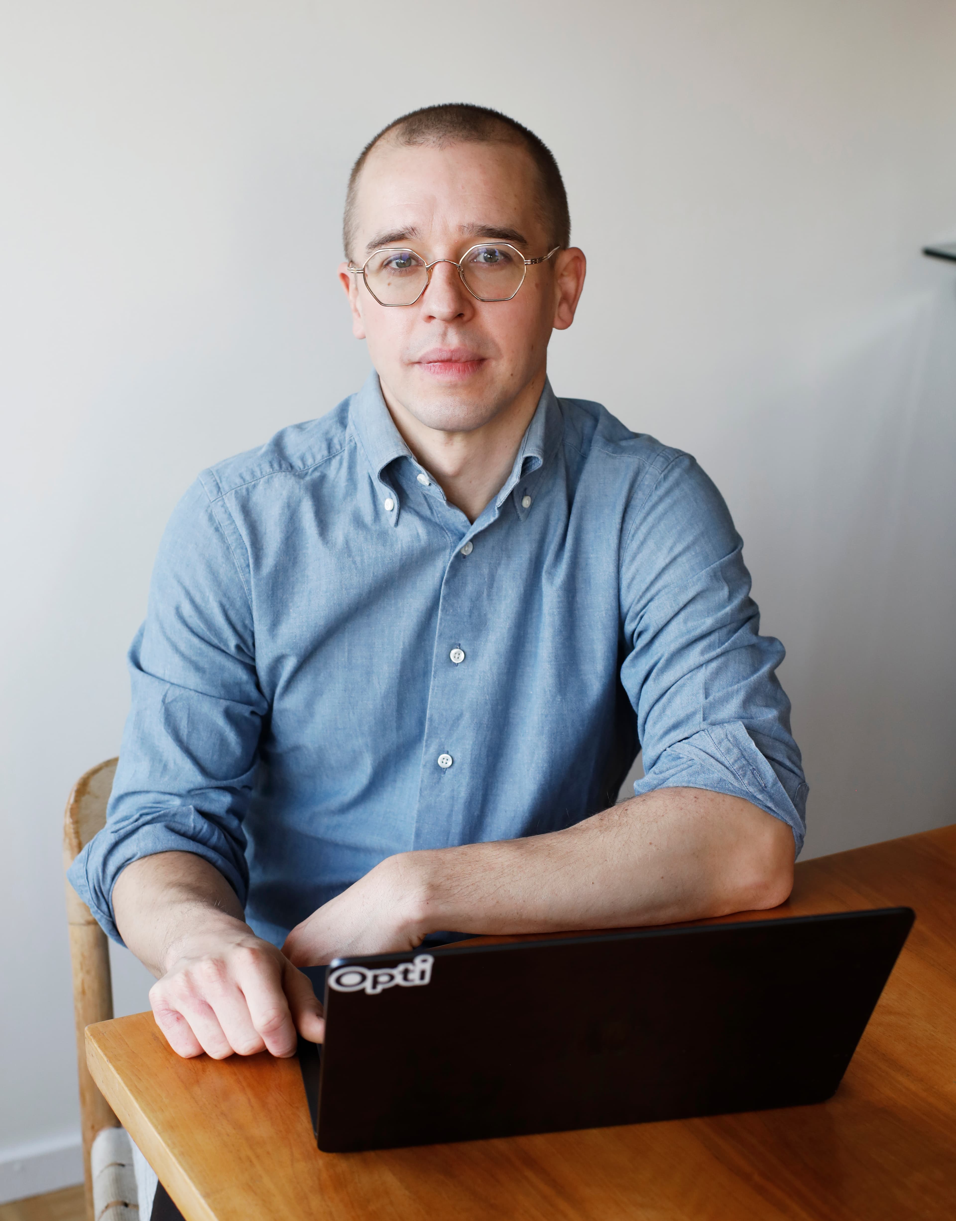 Man med glasgöon, blå skjorta som sitter framför datorn vid ett bord.