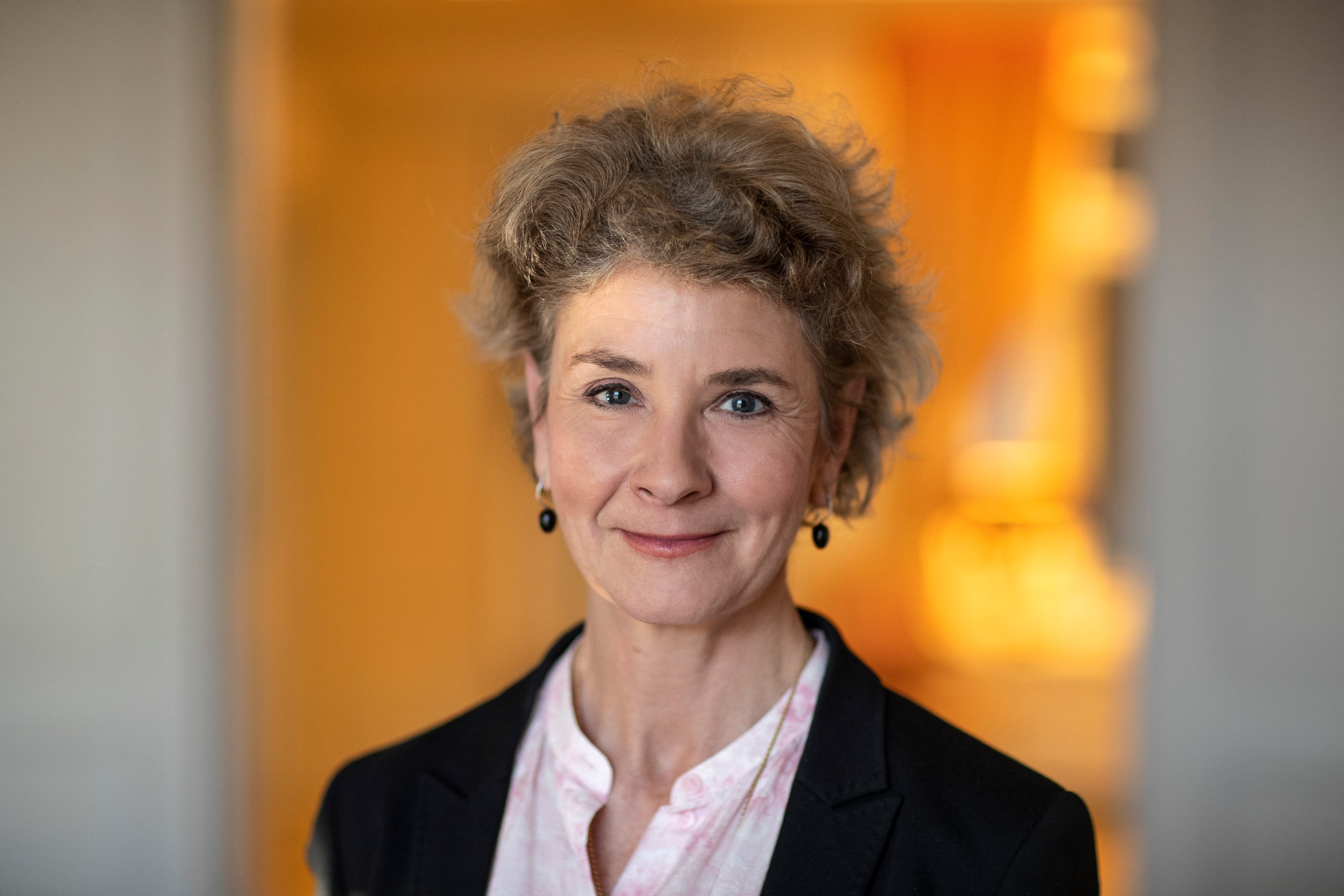 Kvinna med lockigt uppsatt hår, örhängen och svart kavaj.