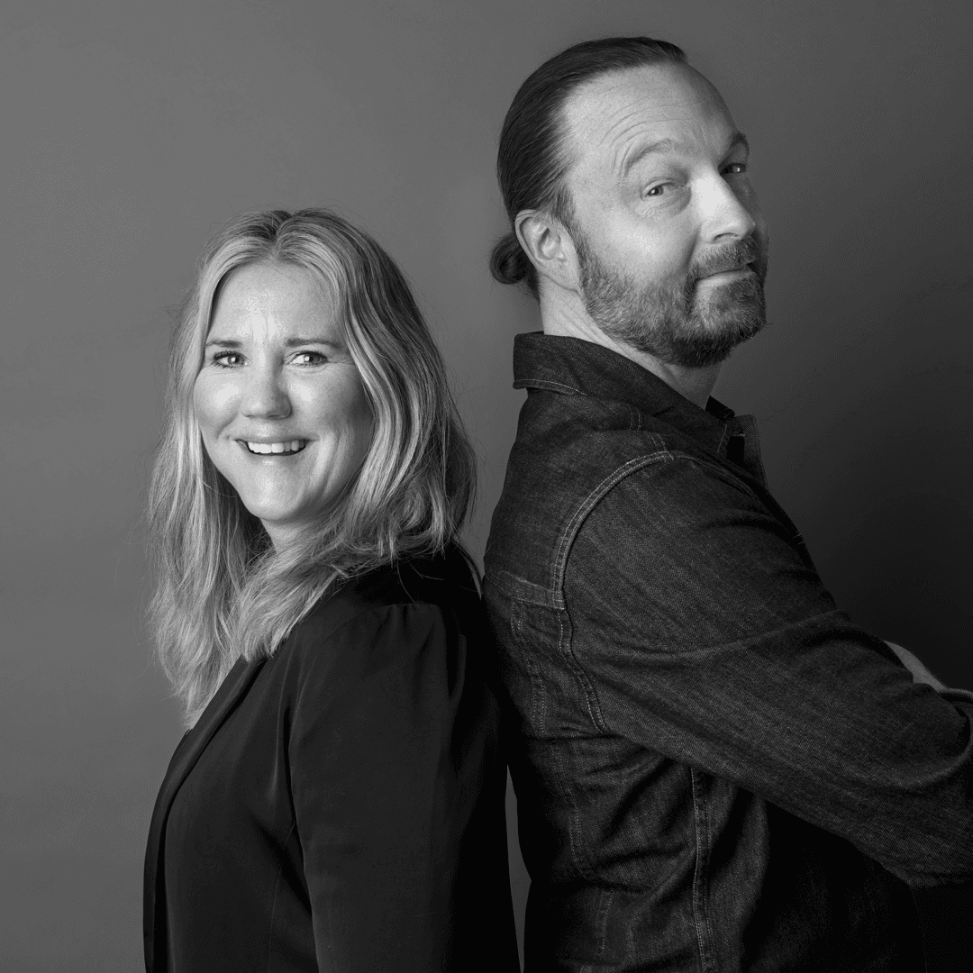 Man och kvinna står rygg mot rygg och ler mot kameran.