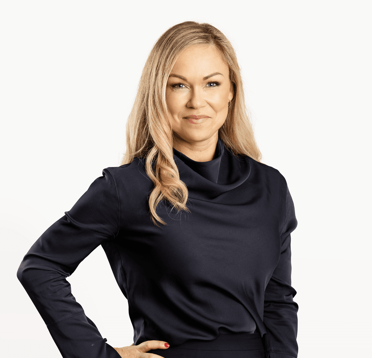 Blond kvinna, klädd i helsvart tittar in i kameran med handen på höften.