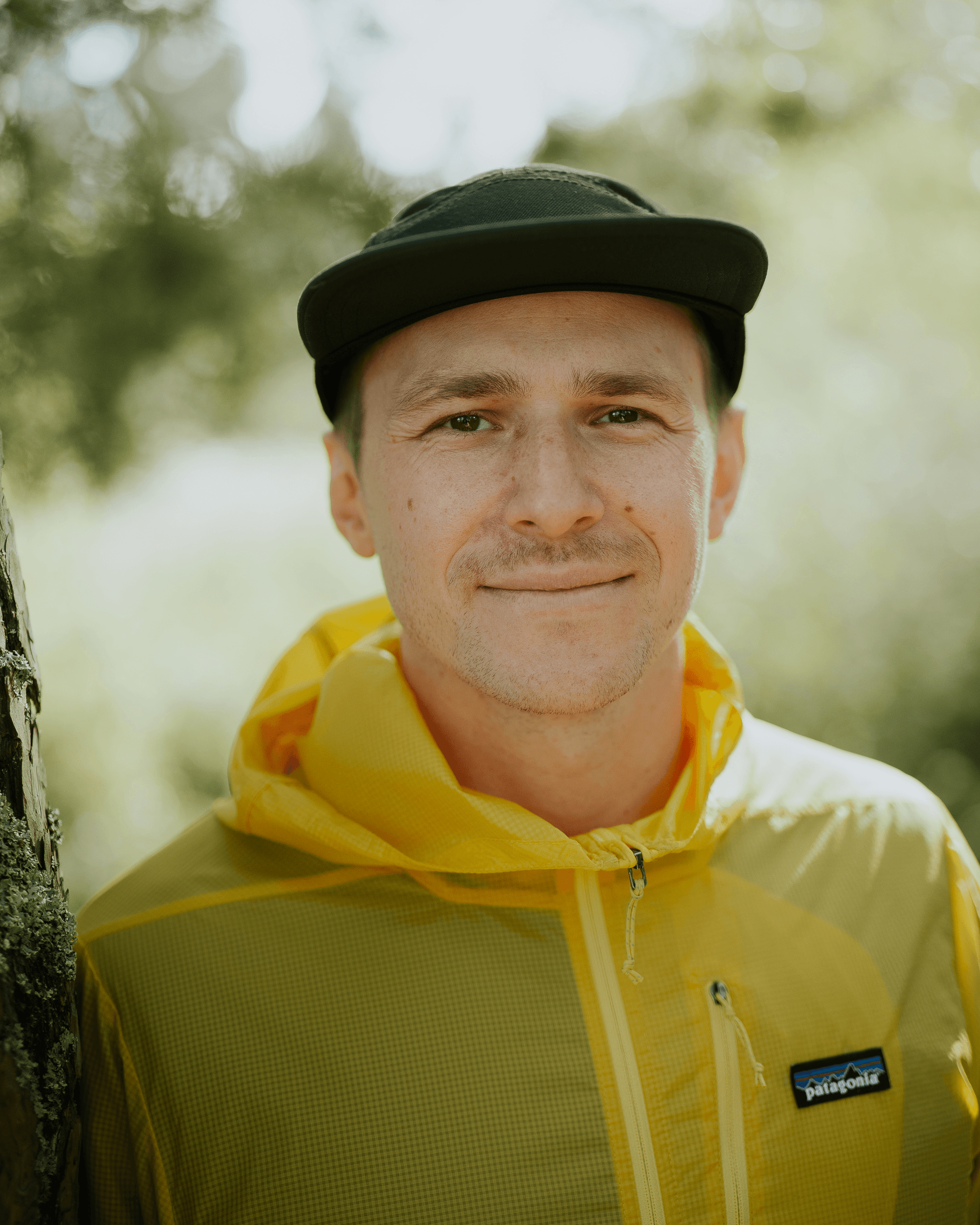 Man i gul jacka och svart keps ler mot kameran