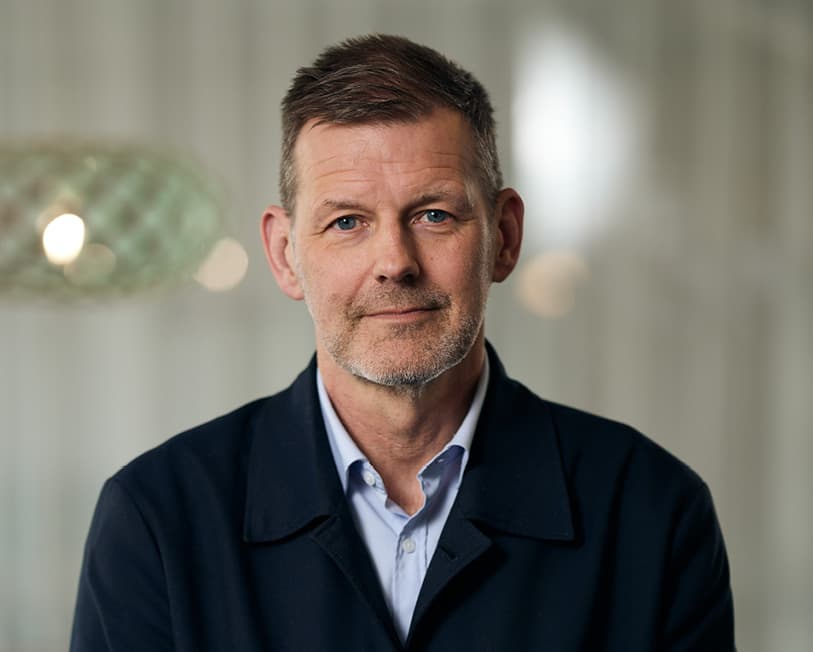 Man med kortklippt hår. Skjorta och mörkblå kofta.