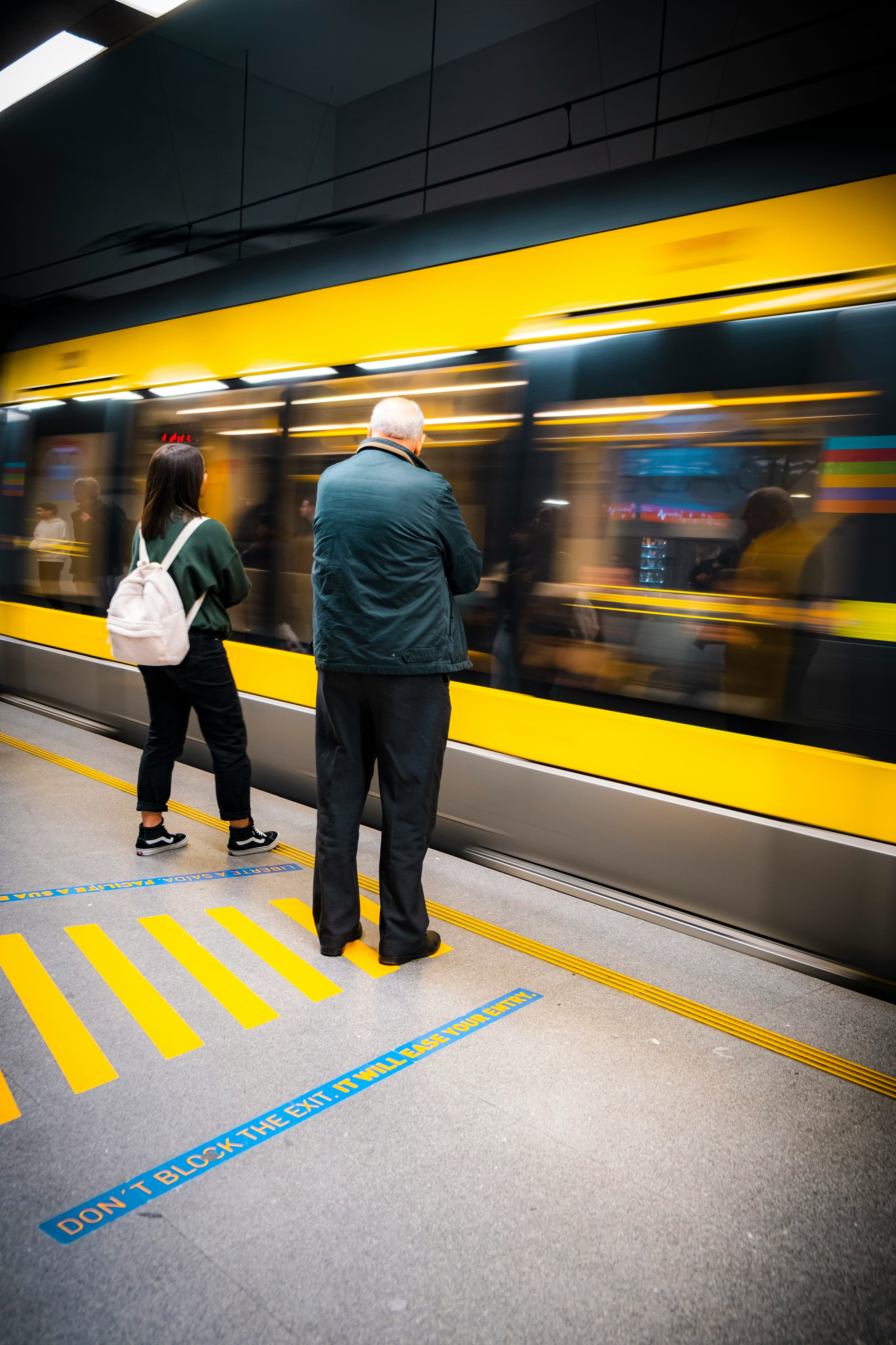 Två personer står vid en plattform när ett tåg rusar förbi.