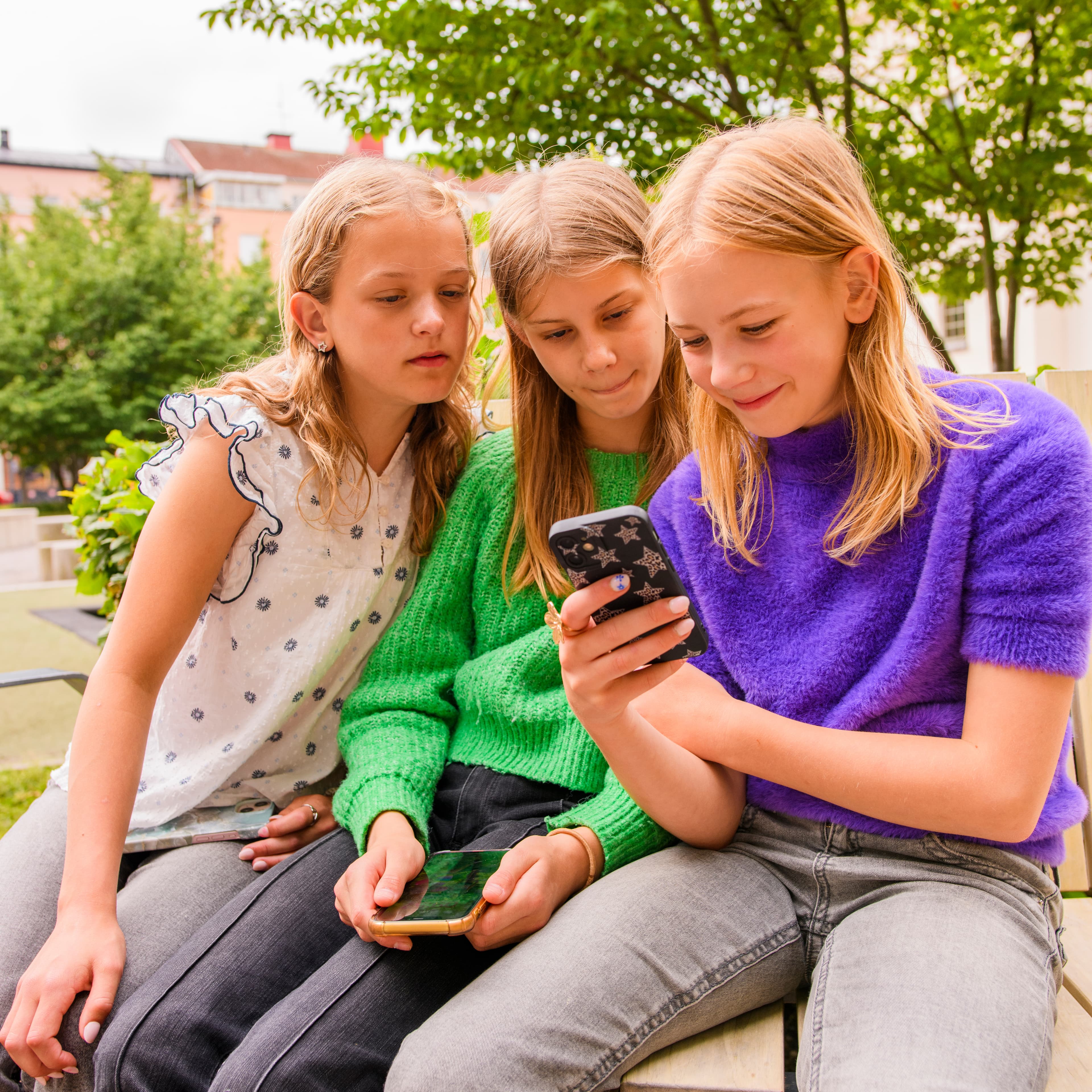 Tre barn sitter och tittar på en mobilskärm tillsammans.