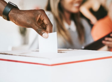 En hand som lägger ner en valsedel  i en vallokal