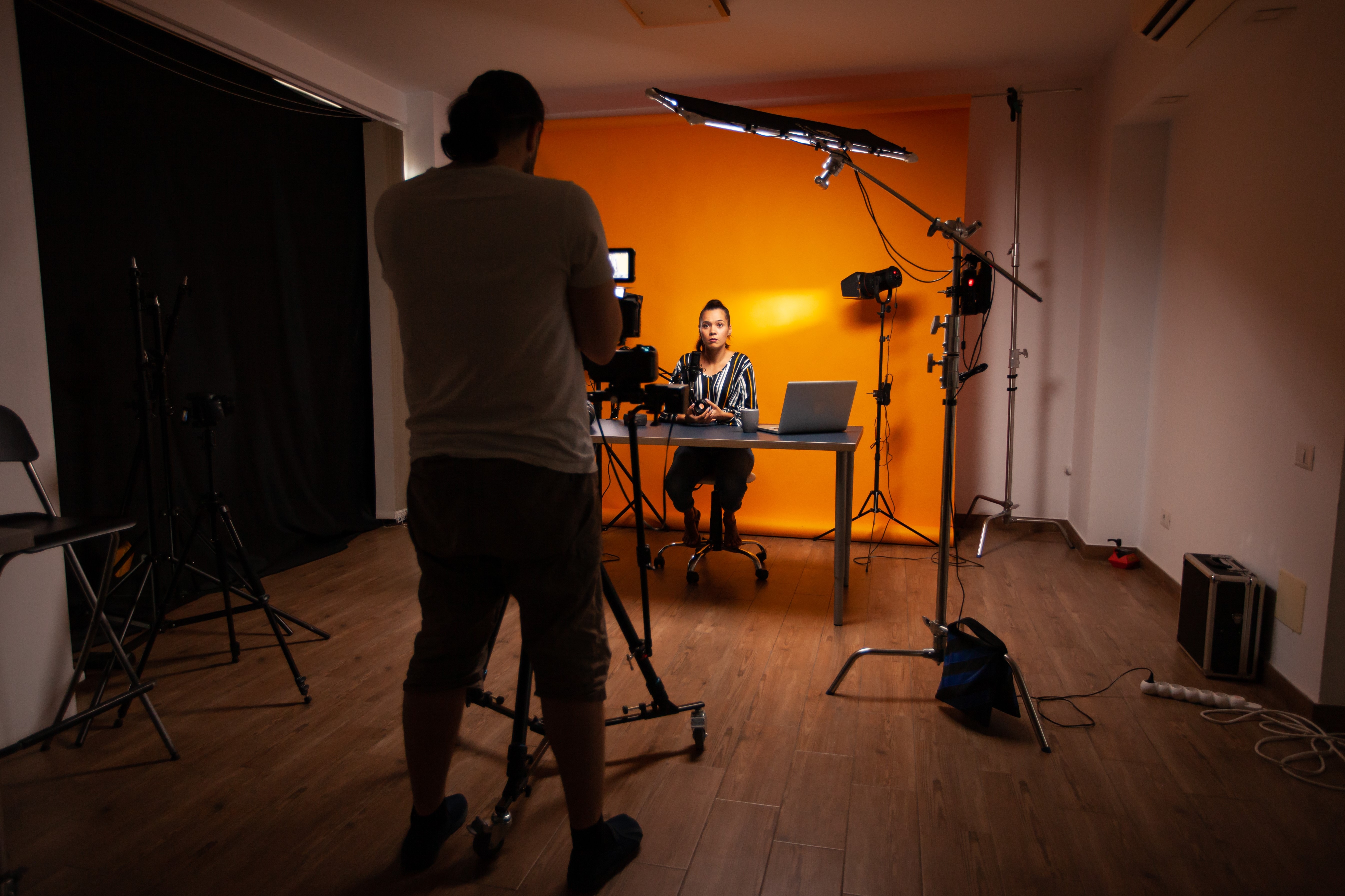 En stående person filmar en annan person som sitter framför en orange vägg
